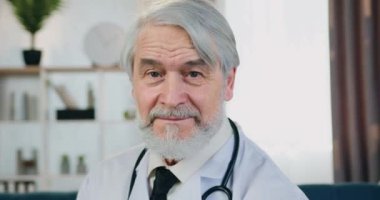 Yakışıklı, gülümseyen, profesyonel, bıyıklı, beyaz önlüklü, kendine güvenen yüz ifadesiyle kameraya bakan doktor portresi.