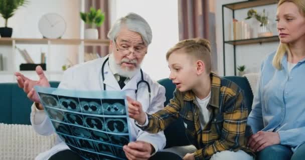 Yakışıklı bir genç, saygın, olgun, sakallı bir doktora ev ziyareti sırasında röntgen filmi hakkında soru soruyor. Çocuklar, anneleri yanlarında oturup konuşmalarını dinliyormuş. — Stok video