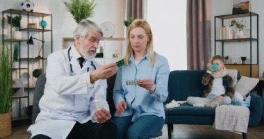 Yakışıklı, hasta, boğaz ağrısı çeken, çay içen ve sorumluluk sahibi, sakallı bir aile doktorunun endişeli annesine haplar vermesi.
