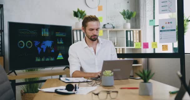 Jovem barbudo experiente e bem-parecido que trabalha no computador na moderna sala de trabalho, trabalha no conceito de escritório — Vídeo de Stock
