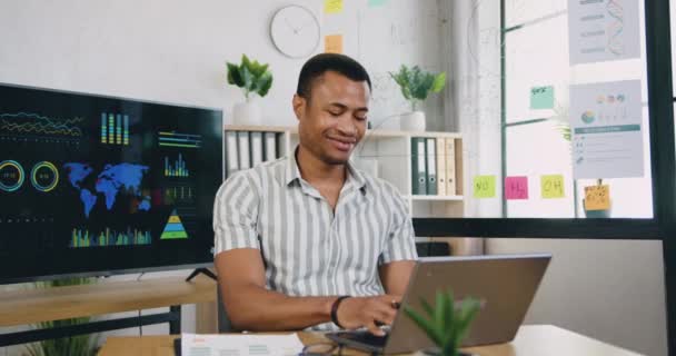 자신 감넘치는 미소를 짓고 열심히 일할 자격 이 있는 아프리카 계 미국인 사무실 직원 이 중요 한 노트를 작성하여 사무실에서 컴퓨터 정보와 함께 일하는 동안보고 한다. — 비디오