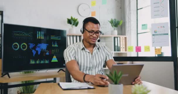 Attraktiv glad leende skicklig afrikansk amerikan i headset arbetar på laptop i moderna kontorsrum och glädje från goda nyheter på bärbar skärm, framgång och lycka koncept — Stockvideo