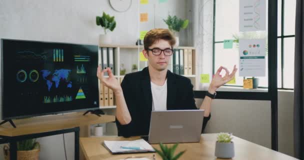 Atractivo relajado exitoso creativo joven gerente de oficina meditando en su lugar de trabajo haciendo una pausa en el flujo de trabajo en la computadora para disfrutar del silencio y la armonía alrededor — Vídeos de Stock