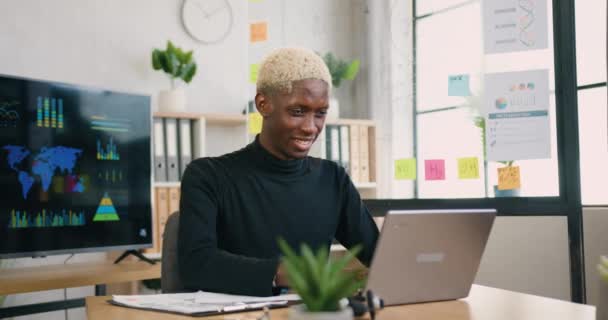 Good-looking smiling satisfied successful young african american guy overjoyed from good news on laptop screen when working in office room,front view — Stock Video