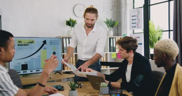 Equipe masculina diversificada altamente qualificada positiva provável do sucesso que trabalha junto na sala de escritório moderna e obtém aquainted com estatísticas do relatório financeiro durante a reunião — Vídeo de Stock