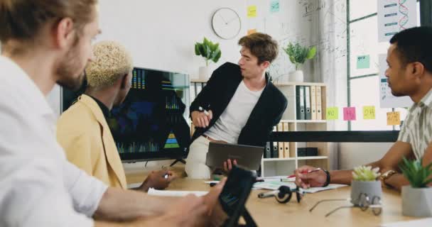 Fešák sebevědomý úspěšný mladý muž kancelářský manažer vysvětlující prezentaci na interaktivním monitoru pro koncentrované multietnické mužské kolegy během setkání v kanceláři — Stock video