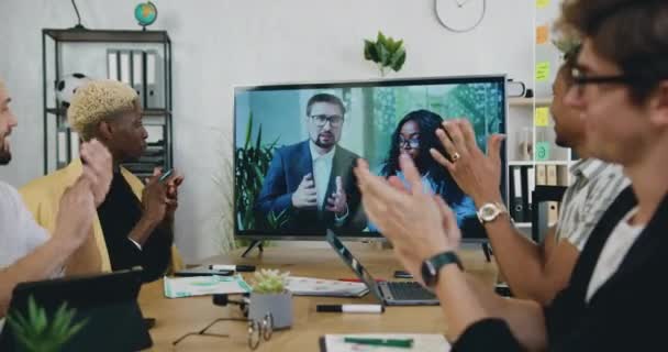 Flujo de trabajo de oficina donde agradable positivo satisfecho experimentado joven diversos colegas masculinos aplaudiendo de la mano después de terminar con éxito videoconferencia con socios internacionales masculinos y femeninos — Vídeos de Stock