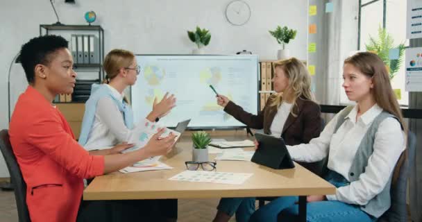 Brainstorming di un team multirazziale di quattro donne, impegnate in incontri di discussione e formazione al tavolo delle conferenze — Video Stock