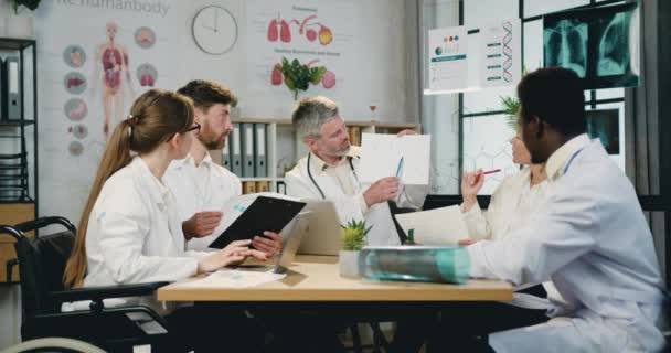 Arbeitsablauf in der Klinik, wo sympathisch selbstbewusste, qualifizierte, verantwortungsvolle Ärzte zusammenarbeiten und dem Bericht des bärtigen Chefarztes zuhören — Stockvideo