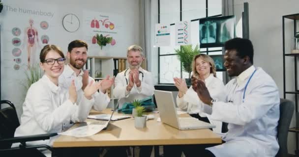 有魅力的快乐微笑的医学概念合格的多文化的男医生和女医生坐在诊所的工作场所，拍手 — 图库视频影像