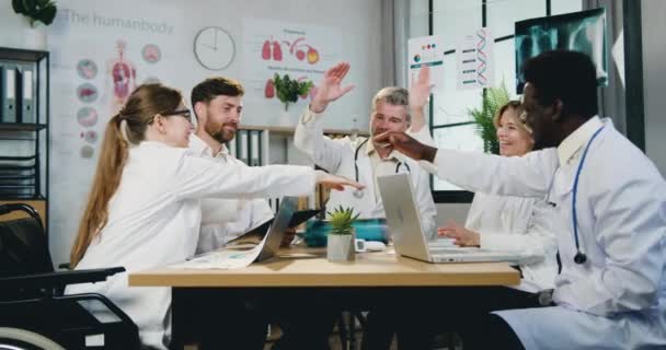 Atractivos médicos de confianza positiva altamente calificados diversos hombres y mujeres haciendo asociación y símbolo de unidad, poniendo sus palmas en las palmas durante la reunión en el taller — Vídeos de Stock