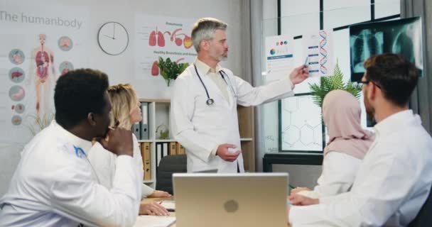 Atraente confiante experiente barbudo médico explicando a estrutura do dna para motivado concentrado qualificados diversos colegas masculinos e femininos durante reunião no consultório da clínica — Vídeo de Stock