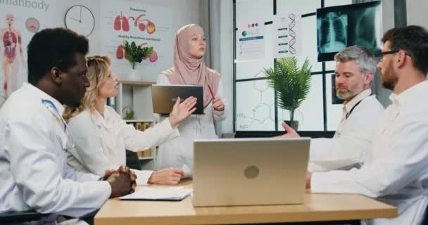 Flux de travail dans une clinique où des médecins masculins et féminins multiculturels qualifiés et attrayants discutent entre eux lors d'une réunion dans un atelier moderne — Video