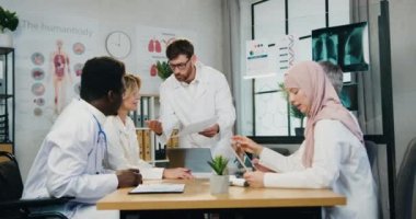 Kızgın, mutsuz, sakallı, başhekim sessiz, korkmuş erkek ve kadın meslektaşlarıyla tartışıyor ve onlara raporlarda hatalar gösteriyor.
