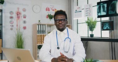 Yakışıklı, olumlu, başarılı, yetenekli, gözlüklü, modern çalışma odasında başparmağıyla poz veren Afrikalı Amerikalı erkek doktorun portresi.