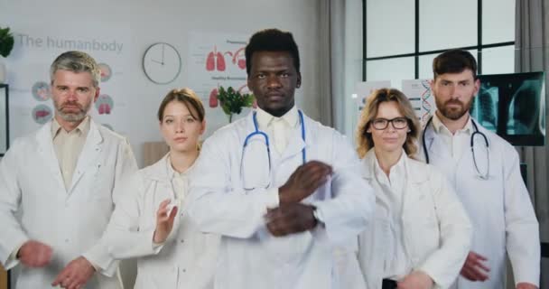 Close up portrait of attractive confident experienced multiethnic medical team which posing on camera with crossed arms in modern hospital workroom — Stock Video
