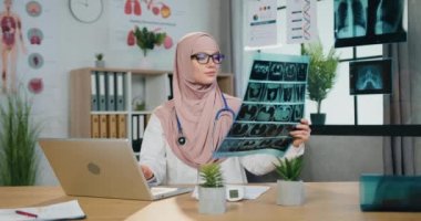 Tıp konsepti, kendinden emin, tesettüre girmiş, tesettüre girmiş, röntgen taramasının sonuçlarını öğrenen ve verileri klinikteki bilgisayara giriş yapan oldukça olumlu bir Müslüman kadın doktor.