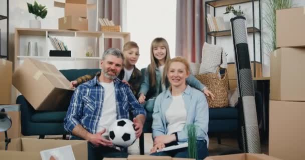Áthelyezés koncepció, ahol vonzó mosolygós fiú és lány átöleli a boldog pozitív szülők és a kamerába a háttérben kartondobozok az új lakás — Stock videók