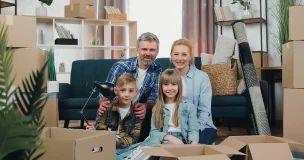 Close up portret pięknej szczęśliwej przyjaznej rodziny, która stanowi przed kamerą z Huggs wśród kartonów po przeniesieniu do nowego mieszkania — Wideo stockowe