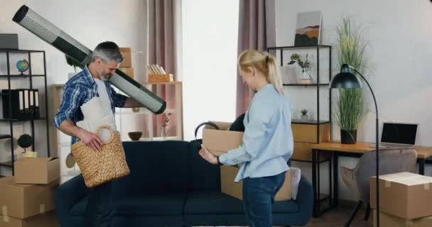 Attrayant heureux sourire couple adulte moderne tenant des boîtes et panier avec décor à la maison et de commencer à meubler leur nouvel appartement après la réinstallation, vue de face — Video