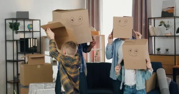 Mänskliga känslor efter flytt där snygga vänliga glada leende familj med två barn dansar i ansiktslådor och efter att ha tagit bort dem krama varandra i rummet — Stockvideo