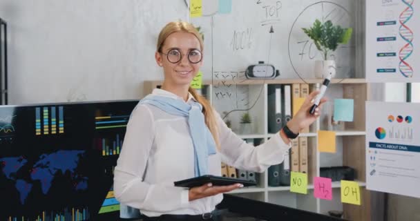 Portré fiatal csinos üzletasszony mosolyog, boldog belenéz kamera közelében üveg tábla háttér, hogy az irodában — Stock videók