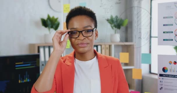 Portrét úspěšné mladé afroamerické ženy s krátkými vlasy a otevřenýma očima při pohledu na fotoaparát, usmívající se. — Stock video