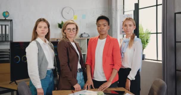 Retrato de quatro multirraciais sérias mulheres de negócios bem sucedidas estão de pé com os braços cruzados sorrindo olhando para a câmera, posando no escritório moderno — Vídeo de Stock