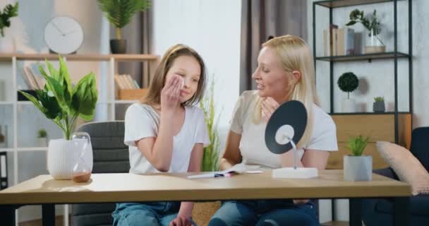 Conceito de procedimentos caseiros cosméticos onde bela mulher loira satisfeita positiva e menina adolescente assistindo no espelho enquanto tira maquiagem usando almofadas de algodão — Vídeo de Stock