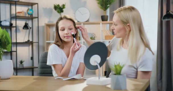 Cute happy smiling teen girl applying blush on face using makeup brush while her caring blond mother watching at her actions,makeup concept — Stock Video