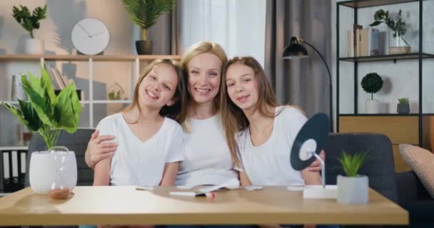 Adorable feliz alegre familia despreocupada de la madre y dos hijas adolescentes que mirando a la cámara con sinceras sonrisas en el acogedor fondo interior del hogar, cámara lenta — Vídeos de Stock
