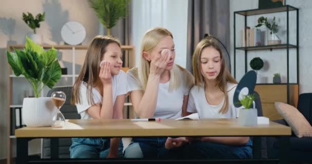 Face huidverzorging concept waar mooie gelukkig positieve blonde vrouwelijke personen als moeder en twee tieners dochters aanbrengen reinigingslotion op het gezicht met katoenen pads — Stockvideo