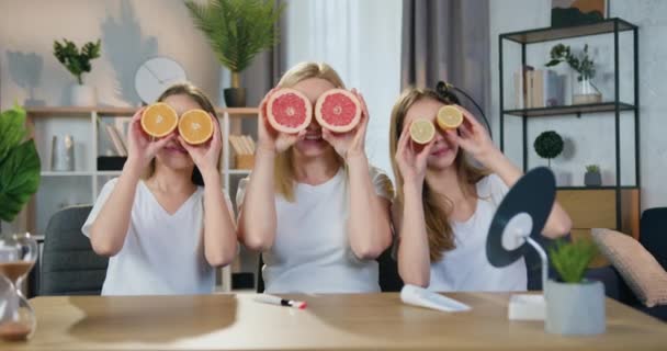 Atraktivní úsměv šťastný hravý blond matka a její dospívající dcery baví doma tím, že polovina citrusů na jejich oči v krásně zdobené obývací pokoj — Stock video