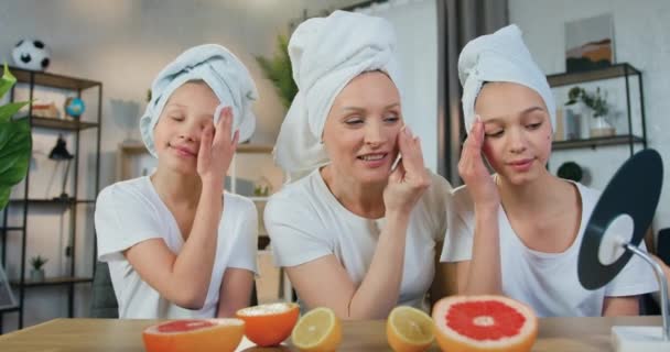 Όμορφη χαμογελαστή ξανθιά μητέρα και οι δύο έφηβες κόρες της με πετσέτες στο κεφάλι κάνοντας επεμβάσεις στο πρόσωπο με βαμβάκι μπροστά από τον καθρέφτη — Αρχείο Βίντεο