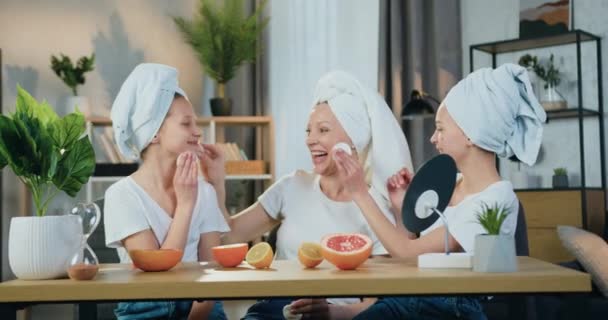 Lovely χαρούμενη χαρούμενη φιλική οικογένεια ως μητέρα και δύο κόρες σε πετσέτες terry απολαμβάνοντας τον ελεύθερο χρόνο τους κατά τη διάρκεια των διαδικασιών του προσώπου με βαμβάκι μαξιλάρια, μπροστινή άποψη — Αρχείο Βίντεο