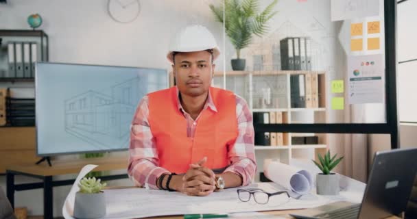 Atrakcyjny, poważny, wykwalifikowany architekt w kamizelce i twardym kapeluszu pozujący przed kamerą w swoim miejscu pracy w nowoczesnym biurze projektowym, z przodu, w zwolnionym tempie — Wideo stockowe