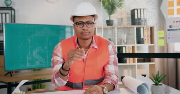 Aangename zelfverzekerde slimme ervaren man-architect in vest en helm die zijn bril afdoet terwijl hij in de camera kijkt in modern design kantoor, vooraanzicht — Stockvideo