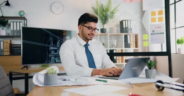 Snygg leende säker kvalificerad skäggig arbetare i glasögon sitter framför datorn och skriva på tangentbord i moderna kontorsrum på dagtid — Stockvideo