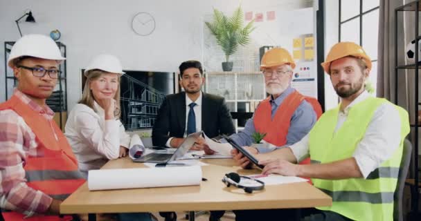 Retrato de atractivo equipo multiétnico serio confiado respossible de ingenieros con capataz que se sienta delante de la cámara en la sala de reuniones en la oficina de diseño — Vídeo de stock