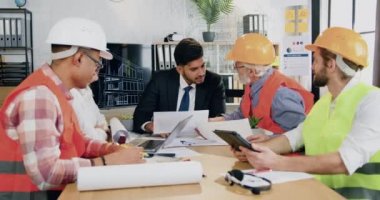 Mühendislik bürosunda çalışan yetenekli sakallı ana mühendis profesyonel erkek ve kadın mühendislerle toplantı odasında soruları tartışıyor.