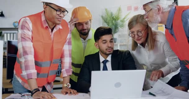 Aantrekkelijke professionele diverse mannelijke en vrouwelijke team van bouwspecialisten herzien buidelproject op laptop samen met succesvolle hoofdarchitect en begroeten elkaar met applaus — Stockvideo