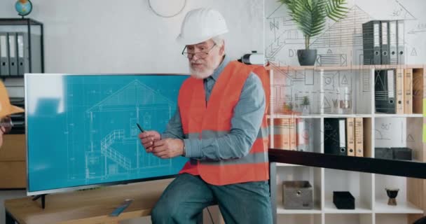 Attractive smiling satisfied experienced mature bearded architect in helemt and vest explaining presentation on digital display and clapping hands together with another male and female architects — Stock Video