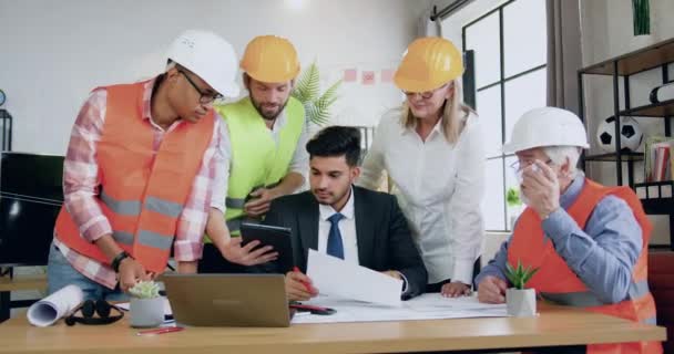 Concepto de la industria de la construcción donde agradable éxito positivo experimentado equipo masculino y femenino de ingenieros de pie cerca de su ingeniero principal barbudo confianza profesional durante la reunión conjunta — Vídeo de stock