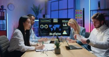 Ekonomistlerden oluşan başarılı, başarılı, çok kültürlü bir ekibin akşamları bilgisayarlarla ilgili çizelgeler ve bilgilerle birlikte çalıştığı ofiste çalışmak.