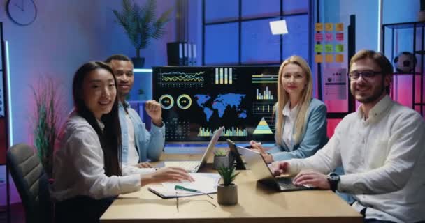 Close up portret sympatyczny uśmiech zadowolony udanych wielonarodowych kolegów z pracy, które gestykulując kciuki w górę do kamery podczas siedzenia za stołem w nowoczesnym biurze wieczorem — Wideo stockowe