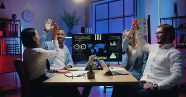 Kantoordoelen concept waar aantrekkelijke glimlachende zelfverzekerde ervaren jonge diverse kantoormedewerkers geven high five elkaar tijdens de vergadering in de avondwerkruimte — Stockvideo
