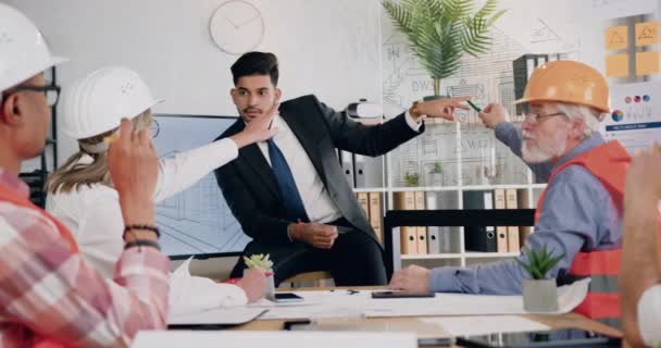 Gerente principal barbudo capacitado de buena apariencia de la compañía de construcción que explica el proyecto en la pared de vidrio para ingenieros-constructores profesionales diversos hombres y mujeres durante la reunión — Vídeo de stock