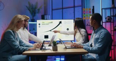 İyi görünümlü, kendinden emin, nitelikli, genç, çeşitli uzmanlardan oluşan bir ekip TV monitöründeki bilgi grafiklerini kullanarak ortak iş stratejisini tartışıyor, akşam ofislerinde birlikte çalışıyorlar.