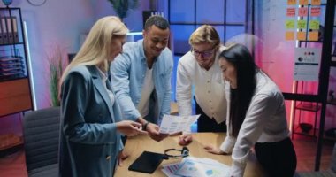 İyi görünümlü, başarılı, deneyimli, çeşitli erkek ve kadın meslektaşlar gece mesaisi sırasında çizelgelerle yapılan araştırmaların sonuçlarını kullanarak ortak projeyi tartışıyorlar.