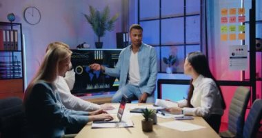 Çekici, kendine güvenen, yetenekli, Afro-Amerikan erkek yöneticinin davranışsal motivasyonlu çeşitli iş arkadaşları için dijital ekranda sunumu açıkladığı akşam ofisindeki çalışma.